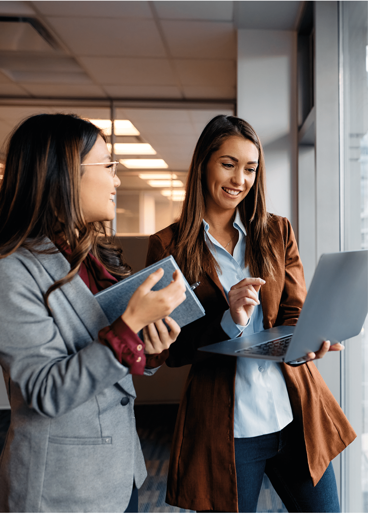 Happy businesswoman and her Asian female colleague using laptop while working in the office.